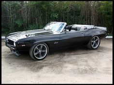 a black muscle car parked in front of some trees