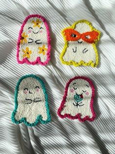 four embroidered ghost appliques on a white bed sheet, each with different colors and shapes