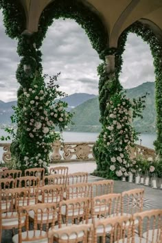 an outdoor ceremony setup with wooden chairs and flowers on the columns, overlooking water in the distance