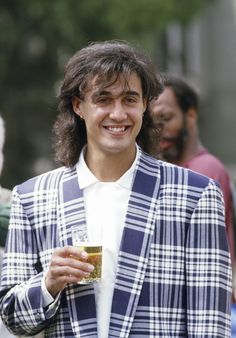 a man with long hair holding a drink in his hand and smiling at the camera