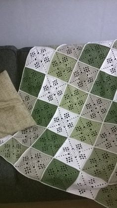 a green and white crocheted blanket sitting on top of a couch next to a pillow