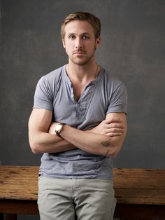 a man with his arms crossed standing in front of a bench and looking at the camera