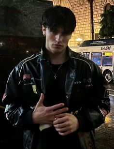 a young man standing in front of a bus on a rainy night with his hands crossed