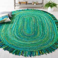 a green rug with fringes on the floor in front of a shelf and potted plant