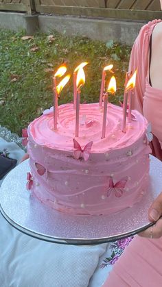 a pink birthday cake with lit candles on it