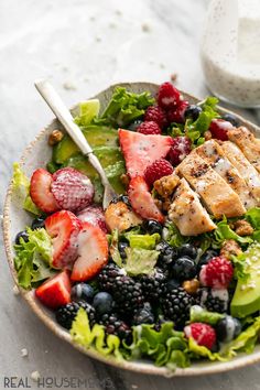 a salad with chicken, berries and dressing in a white bowl next to a glass of milk