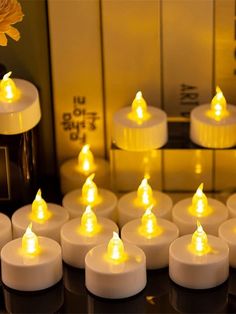 many white candles are lit up in front of a mirror with yellow lights on it