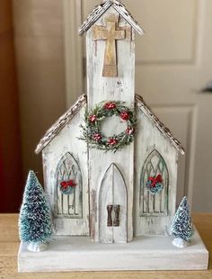 a small white church with wreaths on the front and trees around it, sitting on a table