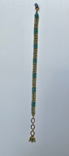 a long beaded necklace is hanging on a white surface with gold and green beads