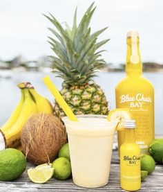 a pineapple, limeade, and coconut drink are on a table next to the water