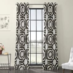 a living room with a white chair and black and white curtains on the windowsill