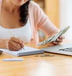 a woman sitting at a desk with a notebook and pen in front of her laptop