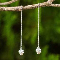 two silver heart shaped earrings hanging from a tree branch with green leaves in the background