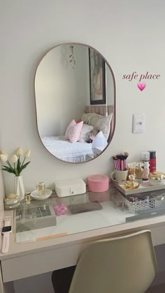 a white desk topped with a mirror next to a chair and vase filled with flowers