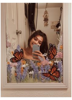 a woman taking a selfie in front of a mirror with butterflies on the wall