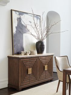 a vase sitting on top of a wooden cabinet next to a table with a chair