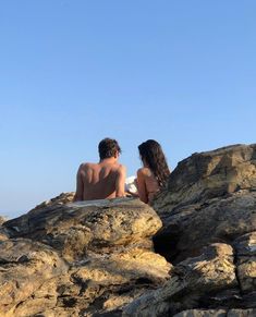 two people sitting on rocks looking out at the ocean