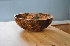 a wooden bowl sitting on top of a wooden table next to a wall in a room