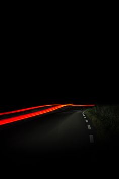 an empty road at night with red light streaks coming from the car's headlights