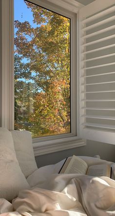 an open book sitting on top of a bed next to a window with trees outside