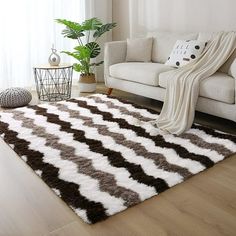 a living room with a white couch, brown and white area rug and potted plant