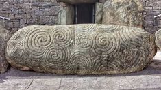 a large rock sitting in front of a stone building with carvings on it's side