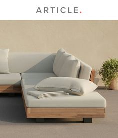 a couch with pillows on it sitting in front of a wall and potted plant