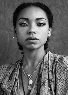 a black and white photo of a woman with necklaces on her neck looking at the camera