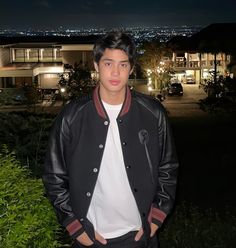 a man standing in front of a building at night with his hands in his pockets