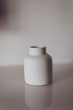 a white vase sitting on top of a table next to a wall in the background