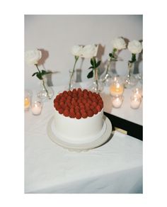 a white cake with red candies on it sitting on a table next to candles