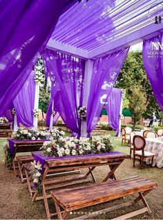 an outdoor wedding setup with purple draping and white flowers on the table, along with wooden benches