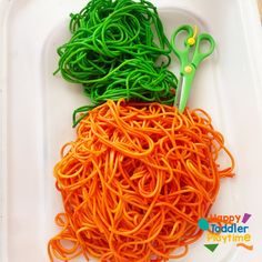 two green and orange scissors sitting on top of a plastic tray filled with spaghetti noodles