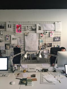 an office cubicle with two computers and several papers on the wall behind it,