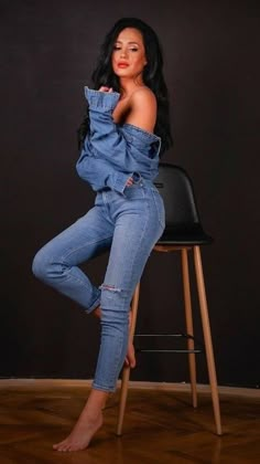 a woman sitting on top of a black chair wearing blue jeans and high heels, posing for the camera