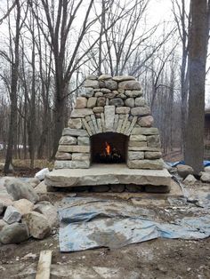 an outdoor fireplace in the middle of some rocks and trees with tarps around it