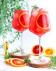 two wine glasses with blood oranges and rosemary garnish on the rim, next to some sliced grapefruit