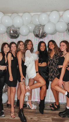 a group of women standing next to each other in front of balloons and disco balls