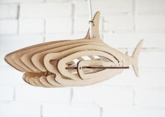 a wooden model of a fish hanging from a hook on a white brick wall background