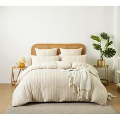 a bed with white sheets and pillows next to a potted plant on a table