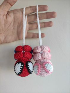 two handmade crocheted ornaments hanging from strings on a white wall next to a person's hand