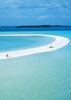 two people are walking on the beach in front of an island with white sand and blue water