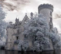 an old castle with snow falling on the ground and trees around it, in front of a cloudy sky