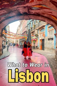 two women walking down a street under an archway with the words what to wear in lisbon