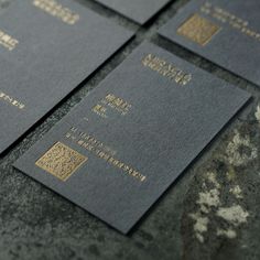 four black and gold business cards sitting on top of each other in front of a stone wall