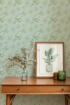 a wooden table topped with a vase filled with flowers next to a wallpapered wall