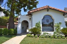 a white house with red tile roof and arched windows in the front yard, surrounded by greenery