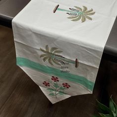 a white table cloth with green and gold designs on it, next to a potted plant