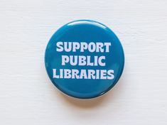 a blue button with the words support public librarians printed on it, against a white background