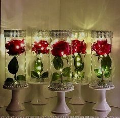 four glass vases with red roses in them on a counter top next to a mirror